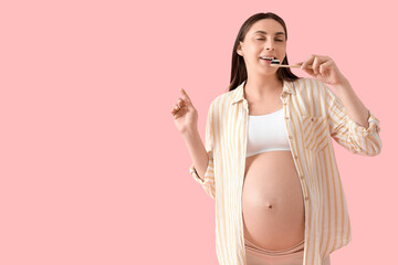 Wall Mural - Young pregnant woman brushing teeth on pink background