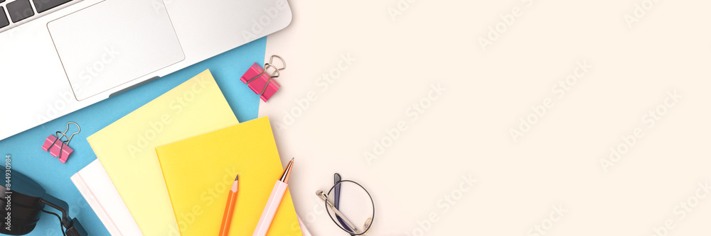 Workspace with laptop and office supplies on a blue and gray background. Banner with copy space.