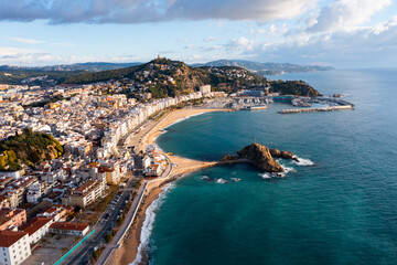 Wall Mural - Scenic drone view of coastal Catalan town of Blanes overlooking white residential buildings and Sa Palomera Rock on background of San Juan hill with ancient castle on sunny day, Barcelona, Spain ..