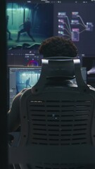 Fototapete - Experienced African American video maker does color grading in program on computer. Process of color correction for movie post production in modern studio. Multiple monitors with action film footage.