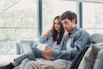 Wall Mural - Millennial couple annoyed by stuck laptop or online news sitting together on sofa, frustrated young angry customers confused by computer problem feeling perplexed or puzzled about email message.