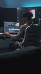 Fototapete - African American multimedia artist drinks coffee and makes color grading in editing program on computer. Process of video post production in modern studio. Multiple monitors with travel movie footage.