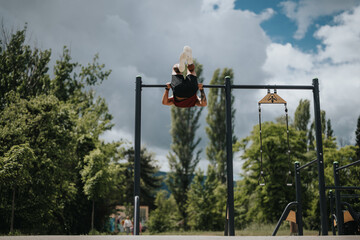 Sticker - A male athlete is captured working out on pull-up bars in a park, demonstrating strength and fitness amidst lush greenery under a cloudy sky.