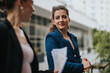 © qunica.com - Confident businesswoman in blue suit talking to colleague outdoors. Professional women having a conversation in urban setting. Business meeting and communication concept.