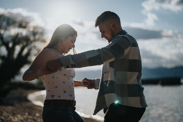 Wall Mural - A joyful young couple dances closely on a sandy beach during sunset, displaying happiness and romance on their holiday trip.