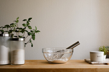 A kitchen countertop with a glass bowl of flour and a whisk on wooden background for cooking, baking, kitchen organization, or minimalist interior design.