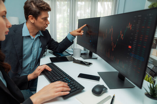 Two business traders analyzing dynamic stock market in currency rate investment program website online on two computer screens, woman checking to compare real time graph at modern office. Postulate.