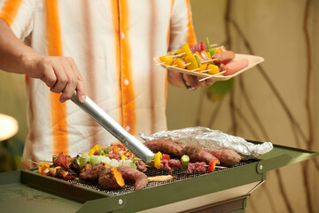 Wall Mural - Hands of man grilling meat and veggies for friends at party