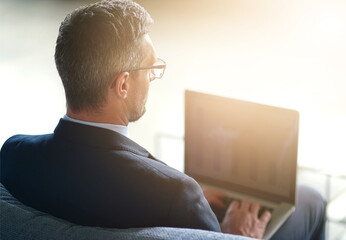 Leinwandbilder - Businessman, glasses and remote work with laptop on sofa, professional website development for company. Male manager, couch and computer with lens flare for digital job, creative designer from behind