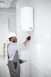 © Serhii - Young African Male Plumber Repairing Boiler