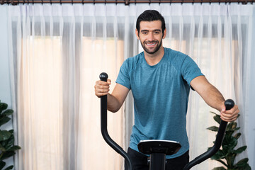 Wall Mural - Athletic and sporty man running on elliptical running machine during home body workout exercise session for fit physique and healthy sport lifestyle at home. Gaiety home exercise workout training.