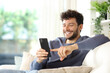 © Antonioguillem - Happy man using smart phone in a house interior