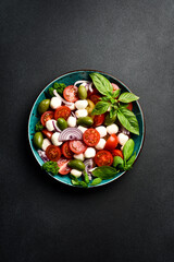 Wall Mural - Caprese salad in a bowl: tomatoes, mozzarella cheese, basil and olives. On a black stone canvas. Minimalism style. Top view.