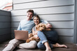 © Westend61 - Happy couple sitting with dog in front of wall