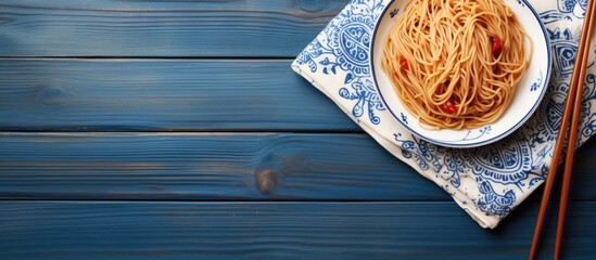 Aufkleber - A top down view of a plate of noodles on a wooden table accompanied by wooden chopsticks set against a blue and white towel Perfect for copy space image