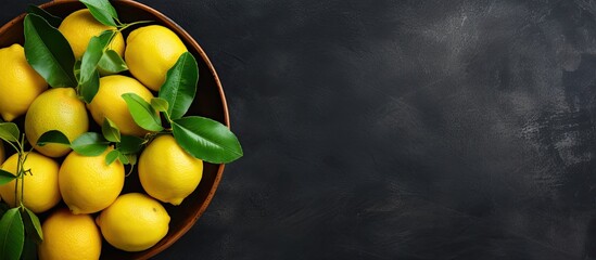 A top down view of lemons arranged in a clay bowl on a dark backdrop creates a food background with plenty of room for additonal elements Copy space image