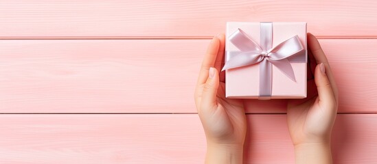 Aufkleber - A top down copy space image depicting a child s hands holding a small blue gift box wrapped with a ribbon It is placed on a pastel pink table top view suitable for occasions like birthdays Valentine