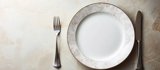 Poster - A white dinner plate sits on a white marble surface featuring intricate patterns A shiny silver spoon completes the composition The image offers ample copy space