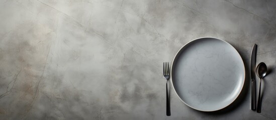Poster - A top down view of a gray stone table with an empty white ceramic plate accompanied by a fork and knife There is ample copy space in the image