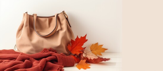 Aufkleber - A seasonal autumn concept featuring a top view of a suede bag cosy scarf and sweater and autumn leaves on a white background in a flat lay composition with copy space image