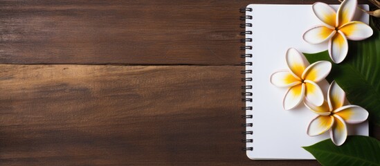 A wooden textured background sets the stage for a Zen aromatherapy concept with a creative arrangement of frangipani flowers and a spiral notebook The notebook provides ample copy space for text