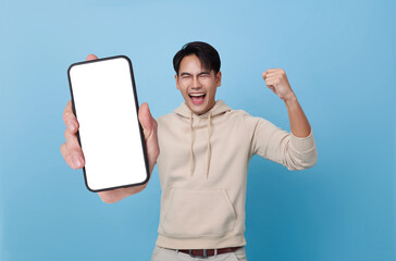 Excited young Asian man showing smartphone with blank screen isolated on blue background.