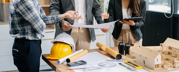 Engineer teams meeting working together wear worker helmets hardhat with on architectural project site and making model house. Asian industry professional team