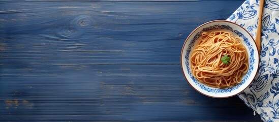 Aufkleber - A top down view of a plate of noodles on a wooden table accompanied by wooden chopsticks set against a blue and white towel Perfect for copy space image