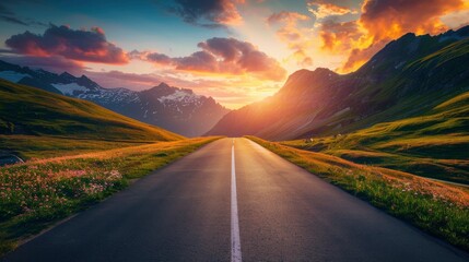 Canvas Print - Empty highway in the middle of flowering hills, steep mountain peaks in the background, sky illuminated by sunset rays, incredible nature