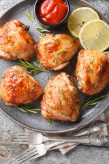 Wall Mural - Traditional baked chicken thighs with lemon and rosemary served with tomato sauce close-up in a plate on the table. Vertical top view from above