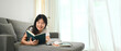 © Prathankarnpap - Happy young asian woman lying on couch and reading book spending leisure time at home