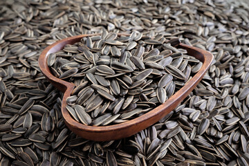 Close-up a heart shaped wooden bowl with striped sunflower seeds.