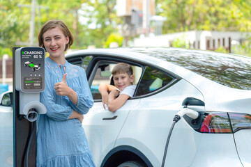 Wall Mural - Environmental awareness family with eco-friendly electric car recharging battery from home EV charging station with little boy inside the car. Rechargeable and EV car technology. Perpetual