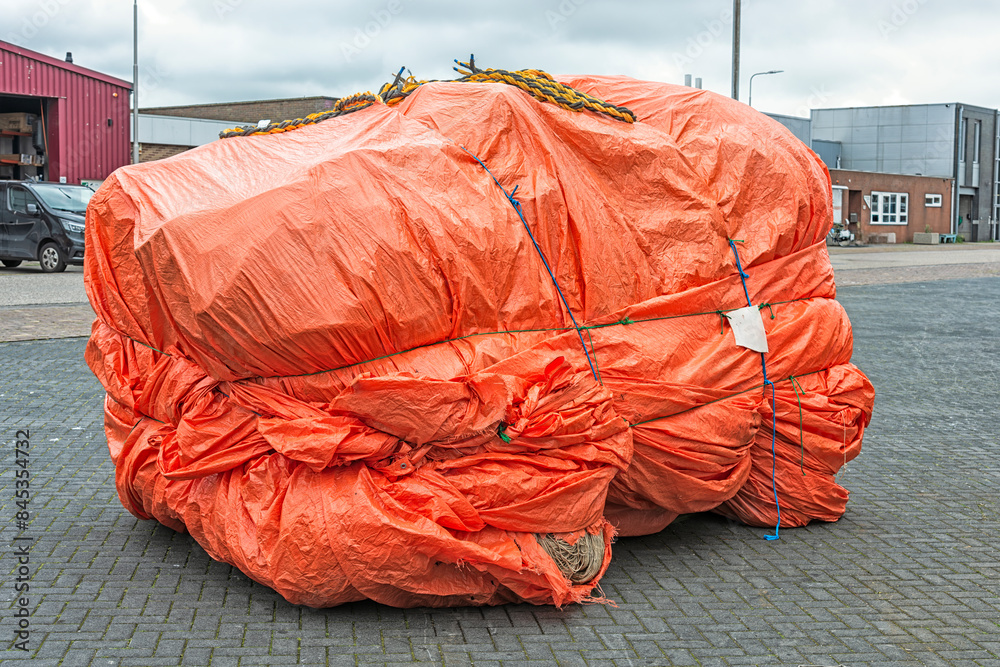 fishing nets wrapped in a large orange tarpaulin tied with ropes