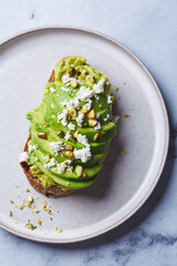 Wall Mural - Avocado toast with feta and pistachio on plate, white marble background.