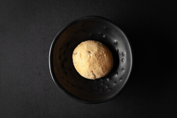Wall Mural - piece of coconut butter bakery cookie, placed in a black bowl on a black background.