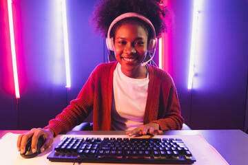 Wall Mural - Gaming streamer, African girl playing online fighting with Esport skilled team wearing headphones in neon color lighting room. Talking other players planing strategies to win competitors. Tastemaker.