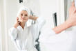 © brizmaker - Mature woman standing in front of mirror, wearing a bathrobe and towel after shower