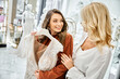 © LIGHTFIELD STUDIOS - Two young women, a bride and her mother, browsing through elegant dresses in a store, contemplating choices for the wedding.