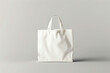 © thebeststocker - White tote shopping bag displayed on a plain light gray background. Realistic illustration for you design