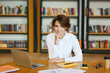 © ViDi Studio - Young confident smiling successful smart employee business woman she wear white shirt casual clothes sit work at library office desk with laptop pc computer looking camera. Achievement career concept.