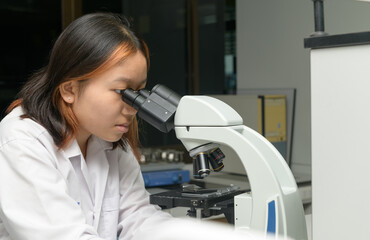 Wall Mural - cute scientist schoolgirl in lab coat looks through microscope for study microbiology in laboratory.