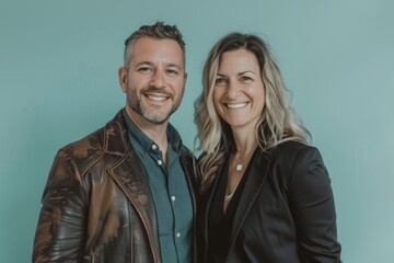 Wall Mural - Portrait of a smiling couple in their 30s sporting a stylish leather blazer isolated in soft teal background