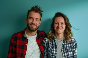 Wall Mural - Portrait of a jovial couple in their 30s dressed in a relaxed flannel shirt isolated in soft teal background