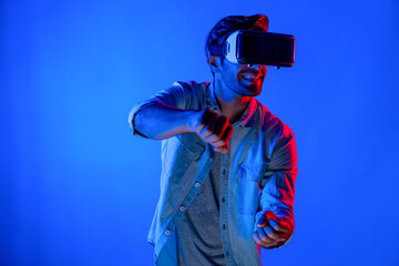 Smart man wear virtual goggle while move driving car hand gesture. Caucasian teenager using futuristic digital technology to enter virtual world while standing at colorful neon background. Deviation.