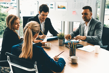 Businessman executive in group meeting discussion with other businessmen and businesswomen in modern office with coffee cups and documents on table. People corporate business working team concept. uds