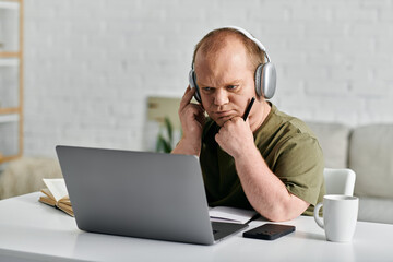 Wall Mural - A man with inclusivity sits at his desk, headphones on, focused on his laptop screen.