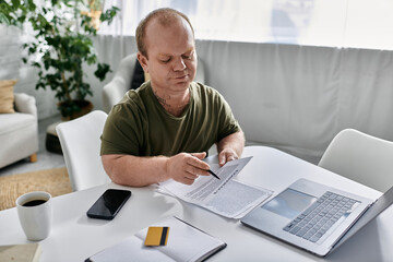 Wall Mural - A man with inclusivity sits at a table in his home, looking intently at a document.