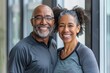 © Markus Schröder - Portrait of a smiling multicultural couple in their 50s wearing a moisture-wicking running shirt in front of sophisticated corporate office background