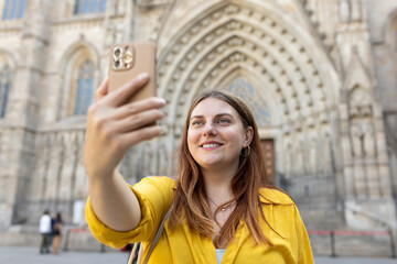 Wall Mural - Young traveling woman taking selfie in front of the famous saint Eulalia church in Barcelona. Concept of travel, tourism and vacation in city. Use technology concept, Traveling Europe